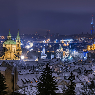 View of Prague, saint Nicolas cathedral, Charles bridge, Zizkov tower and Old town square from Prague Castle view point at night in winter. Roofs covered with snow in the foreground. Prague, Czech Republic