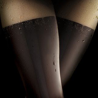 Dark cold beer in two steamed glasses, resembling sexy female legs in black stockings. Black background