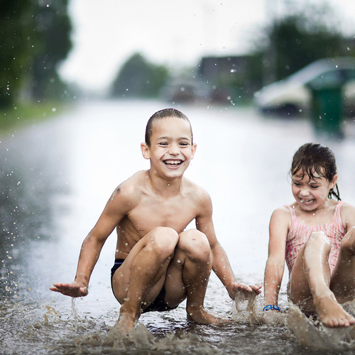 Счастливые дети прыгают в луже во время летнего ливня / Пока они не выросли