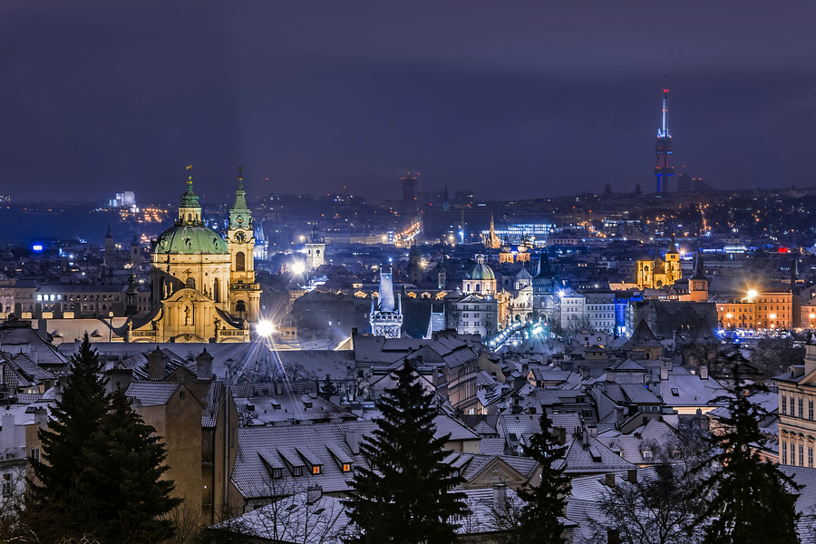 View of Prague, saint Nicolas cathedral, Charles bridge, Zizkov tower and Old town square from Prague Castle view point at night in winter. Roofs covered with snow in the foreground. Prague, Czech Republic