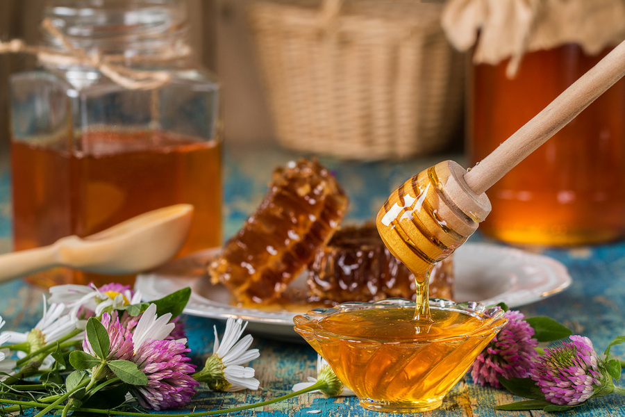 Two honey pots with honeycomb  on a wooden table  with flowers