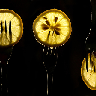 collage of three slices of lemons on the fork on dark black background. silhouette of a fork in the back light. Drops of juice flow down the forks