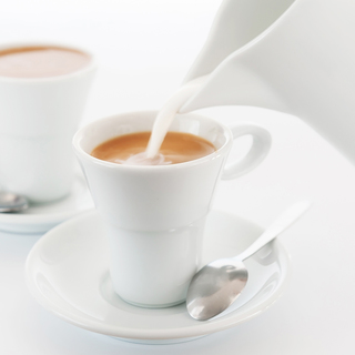 Milk is poured into a cup of coffee. White cups and a milkman on a white background. A large plan. An elective focus.