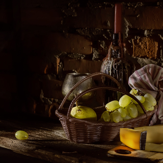 bunch of grapes, pears, cheese, a glass and a bottle with a candle in a wine cellar