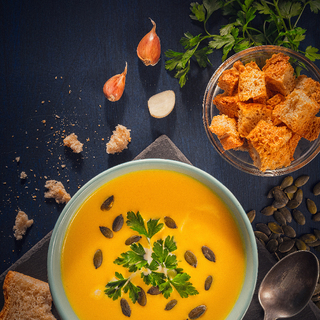 Pumpkin soup, pumpkin seeds and bread on a blue wooden table.