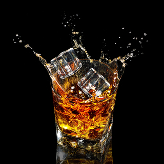 Glass of whiskey with splash on black background