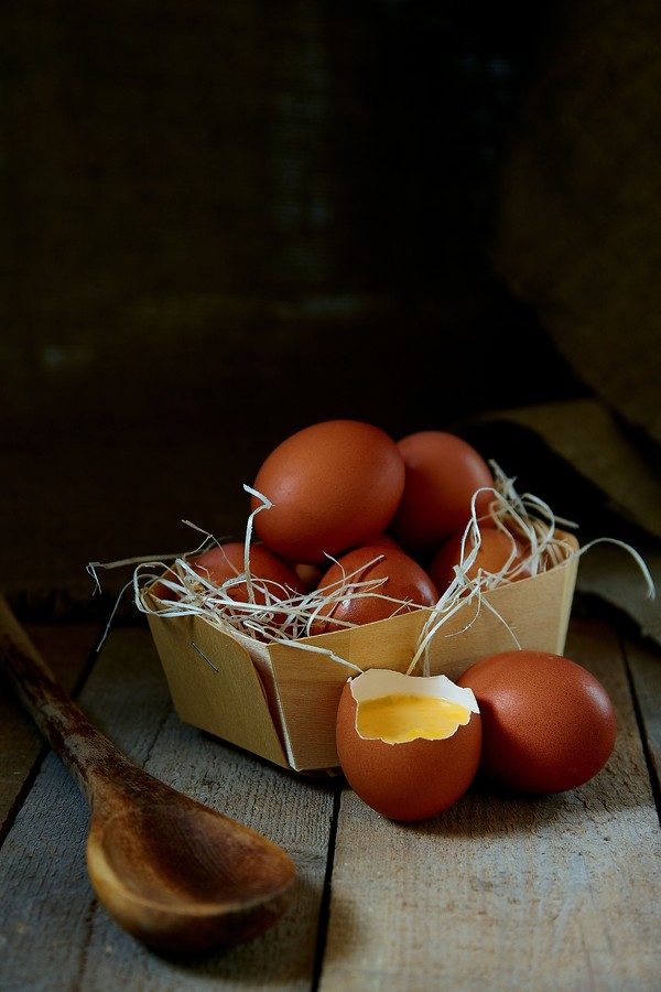 Many village eggs lie in a wicker basket in the chicken coop on the wooden floor.