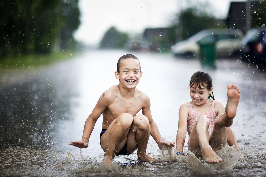 Счастливые дети прыгают в луже во время летнего ливня