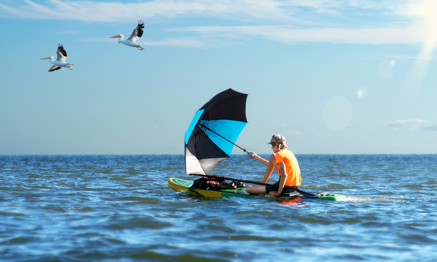 On the paddle board, catching the wind with an umbrella floats a teenager on the sea