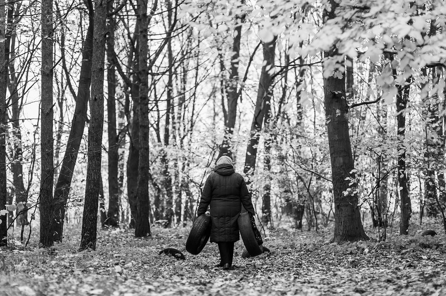 Женщина идет домой и несет с собой старые автомобильные покрышки,чтобы использовать их в хозяйстве и украсить территорию возле ее дома. Могилев,Беларусь
